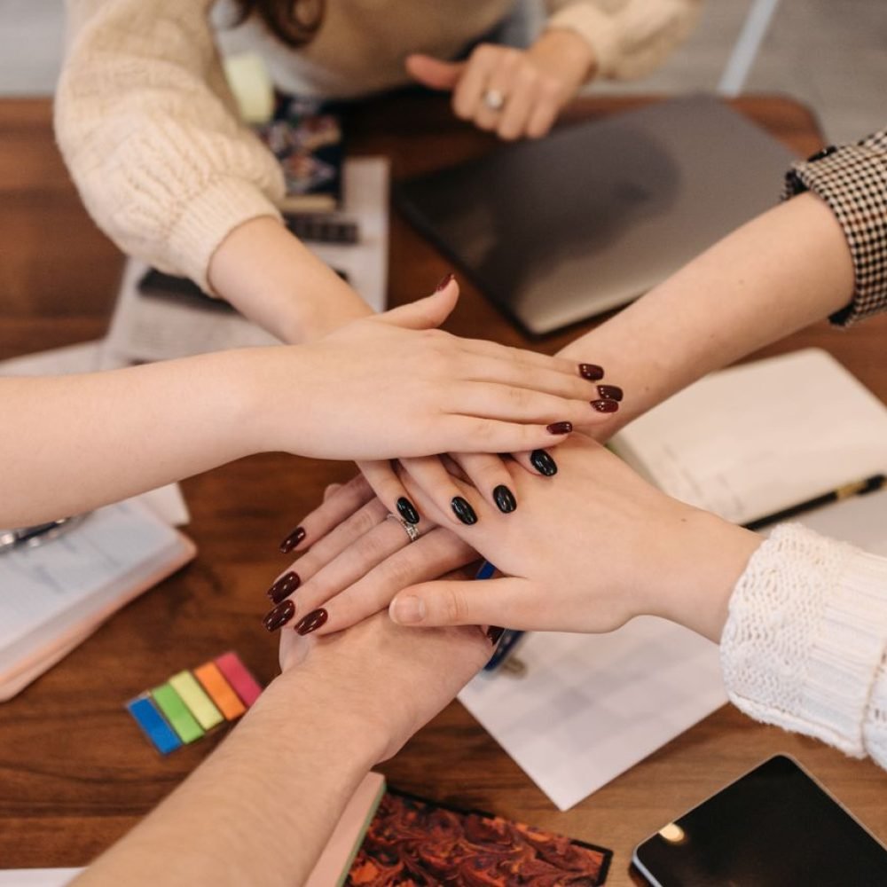 Hands stacked in teamwork gesture over a table with office items symbolizing collaboration.